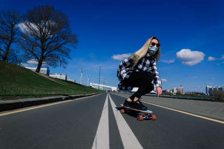 Portrait of a young female in a medical mask with longboard in the city during the quarantine periodの写真素材