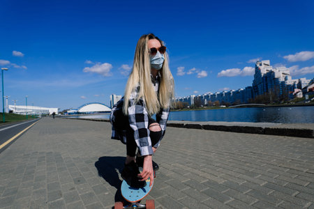 Portrait of a young female in a medical mask with longboard in the city during the quarantine period