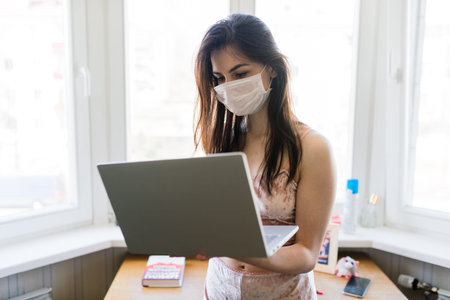 Beautiful dark-haired female in quarantine wearing protective mask and working at home