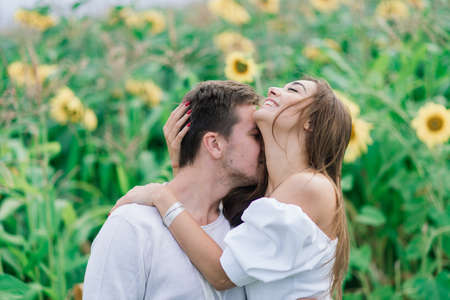 Minsk, Belarus - 08.13.2020. Loving couple in white dresses kissing, smiling, hughing in field of sunflowersのeditorial素材