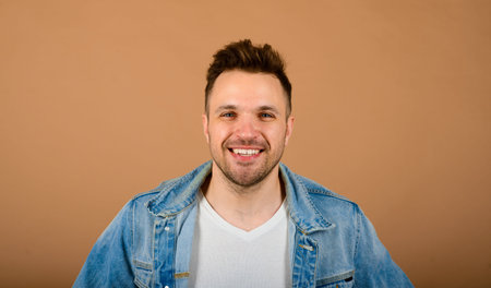 Handsome man standing and smiling isolated on light brown studio background. Male half-length...