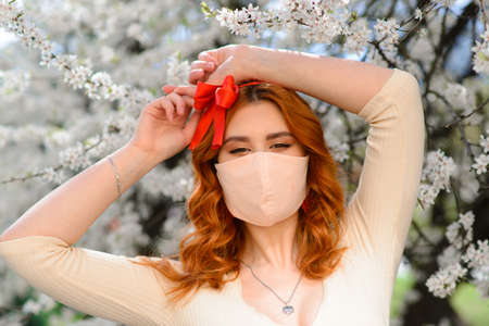 Girl, young woman in a protective sterile medical mask on her face in the spring garden. Pollution, virus, pandemic coronavirus concept.の写真素材