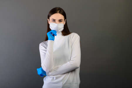 Girl in medical gloves dress a medical mask on her face on a background. Covid-19の写真素材