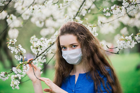 The girl with blue eyes in mask in blossom park. Covid -19. New reality
