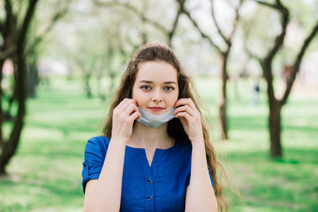 The girl with blue eyes in mask in blossom park. Covid -19. New reality