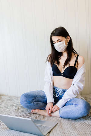 Beautiful dark-haired female in quarantine wearing protective mask and working at homeの写真素材