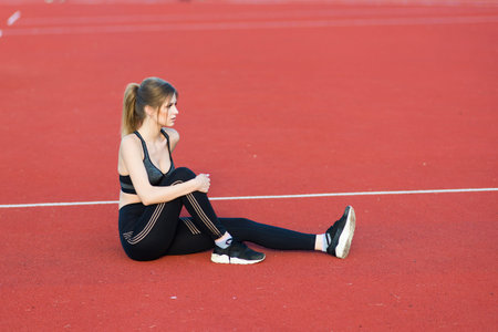 A female coach with dark hair stands on the red running track of the stadium, dressed in sports...