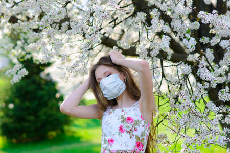 Teenager girl in medical mask in spring flowering garden. Concept of social distance, prevention of coronavirus.の写真素材