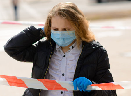 Portrait of sad caucasian child in face mask on closed playground outdoor. Coronavirus social...