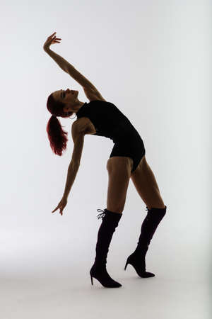 Young beautiful flexible female in a black jumpsuit and high heels is posing in a dance studio.の写真素材