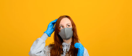 Portrait of a girl in a mask, which puts on rubber gloves. Yellow background.