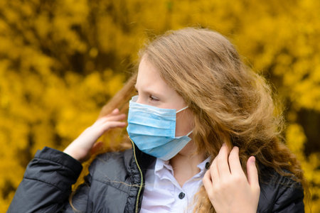Portrait of sad caucasian child in face mask on closed playground outdoor. Coronavirus social...
