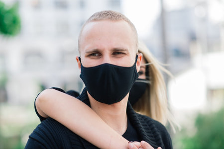 Couple wearing trendy fashionable protective masks, denim jackets, walking in empty street of...