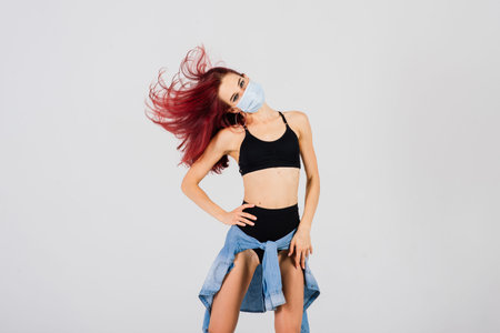 Female dancer in the styles of strip plastic and pole dance with face mask on light background.
