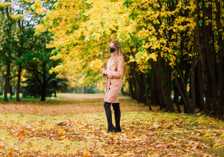 A young woman protecting from corona virus when walking in park. Autumn background.