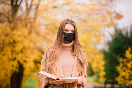 A young woman protecting from corona virus when walking in park. Autumn background.の写真素材