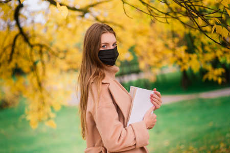 A young woman protecting from corona virus when walking in park. Autumn background.の写真素材