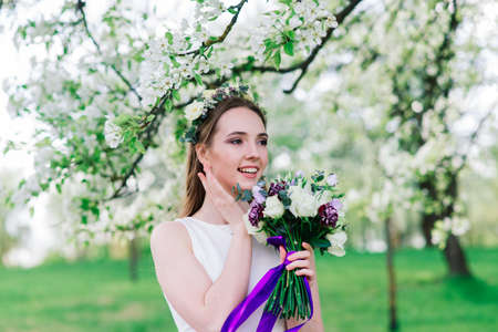 The bride in white wedding dress is holding a bouquet in green park. Summer wedding on a sunny day.の写真素材