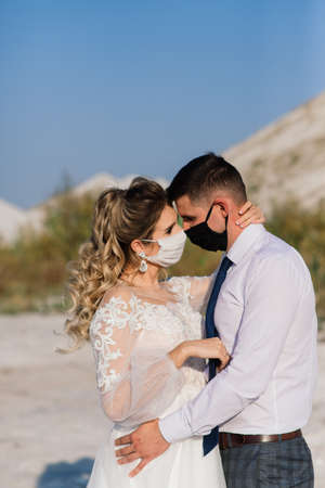 Young loving couple walking in medical masks in the park during quarantine on their wedding day.の写真素材