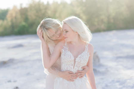 Beautiful lesbian couple walking on sand along a river bank on their wedding dayの写真素材
