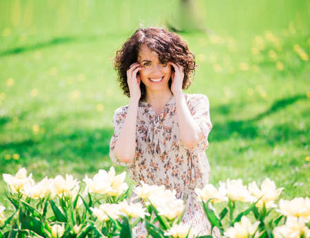 Young attractive woman with curly long hair posing in spring blooming gardenの写真素材