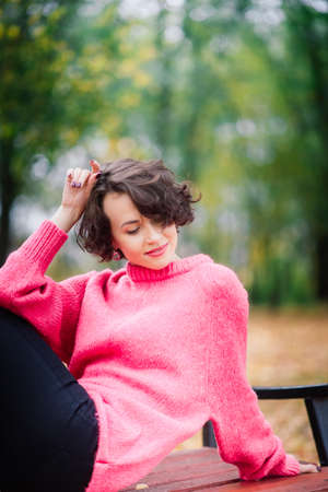 Young beautiful ballerina in fair coat and pointe shoes sit on the bench, rest outdoors in autumn park.の写真素材