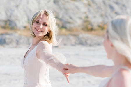 Beautiful lesbian couple walking on sand along a river bank on their wedding dayの写真素材