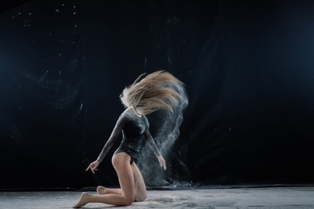 A long-haired girl in a black bodysuit in flour in a black studio.