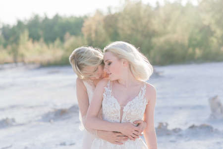 Beautiful lesbian couple walking on sand along a river bank on their wedding dayの写真素材