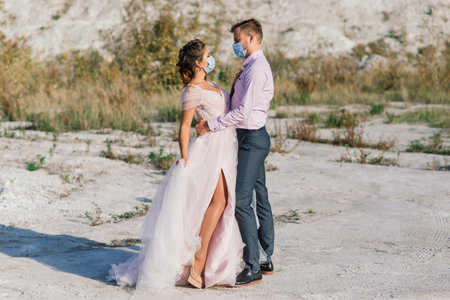 Young loving couple walking in medical masks in the park during quarantine on their wedding day.の写真素材