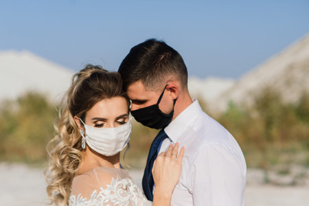 Young loving couple walking in medical masks in the park during quarantine on their wedding day.