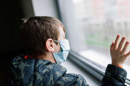 Boy wearing medical face mask looking out deep in thought, protective measures against spreading of Covid-19の写真素材