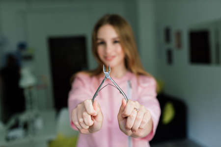 Manicure tools in hands of female manicurist wearing pink uniform in a studioの写真素材