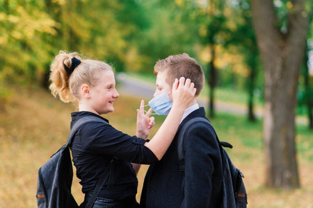 Schoolchildren, boy and girl in medical masks walk in the city park.