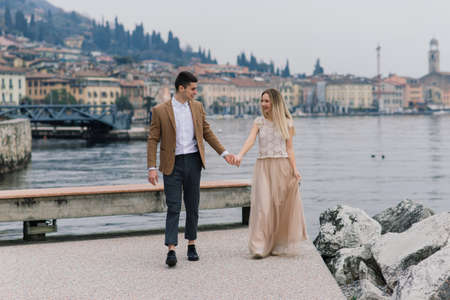 Salo, Italy - 02.02.2020. Romantic young couple sitting on the river dock and walking on the lake bank.のeditorial素材