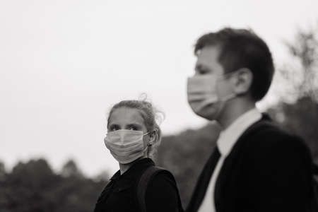Schoolchildren, boy and girl in medical masks walk in the city park.の写真素材