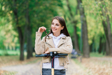 Young woman riding an electric scooter in autumn park. Green transport, traffic jam problems.の写真素材