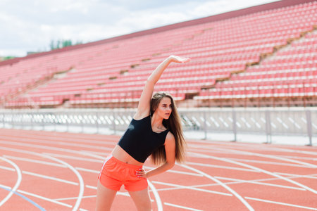 A female coach with dark hair stands on the red running track of the stadium, dressed in sports uniform.の写真素材