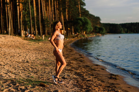 Minsk, Belarus - 07.08.2020. Caucasian fit woman with sport body posing on beach at sunset time. Weight loss by summer.のeditorial素材