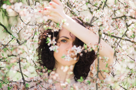 Young attractive woman with curly long hair posing in spring blooming gardenの写真素材