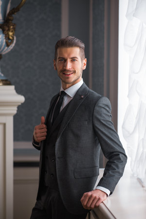 Groom at wedding day smiling and waiting for bride in the hall of the hotel. Elegant rich man in costume and bow-tie.の写真素材