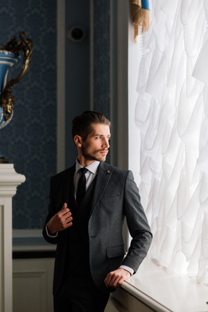 Groom at wedding day smiling and waiting for bride in the hall of the hotel. Elegant rich man in...