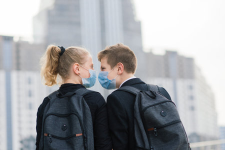 Schoolchildren, boy and girl in medical masks walk in the city.
