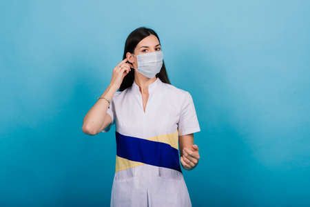 Portrait of female doctor in a medical mask looking away isolated on blueの写真素材