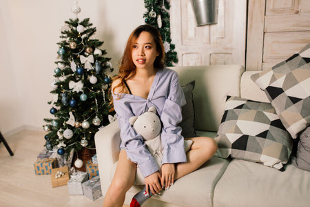 Beautiful young asian woman celebrating christmas at home, having fun opening presents