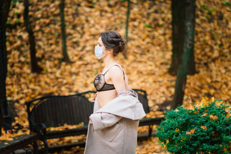 Fashion portrait of sexy woman in face mask and a bodysuit in autumn park.の写真素材