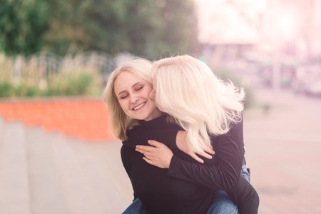 Two young females walking smiling embracing and kissing outdoorの写真素材