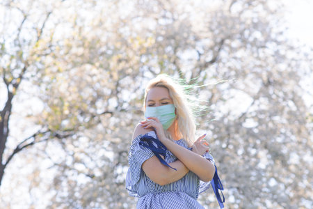 A girl in a protective medical mask in the spring among the blooming garden. . Spring allergy and covid concept.の写真素材