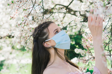 A girl in a protective medical mask in the spring among the blooming garden. . Spring allergy and covid concept.の写真素材