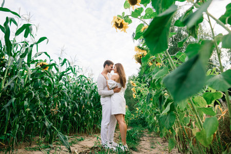 Minsk, Belarus - 07.08.2020. Beautiful gorgeous woman and stylish handsome male, rustic couple in a sunflower field kissingのeditorial素材